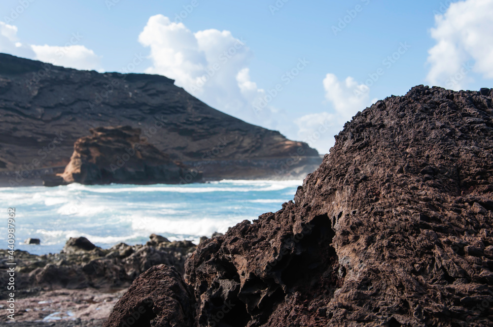 Kanaren, Lanzarote,. Küstenlinie mit typischen schwarzem erkaltetem Lavafelsen und kräftiger Brandung. Im Hintergrund die typische vulkanische  Landschaft