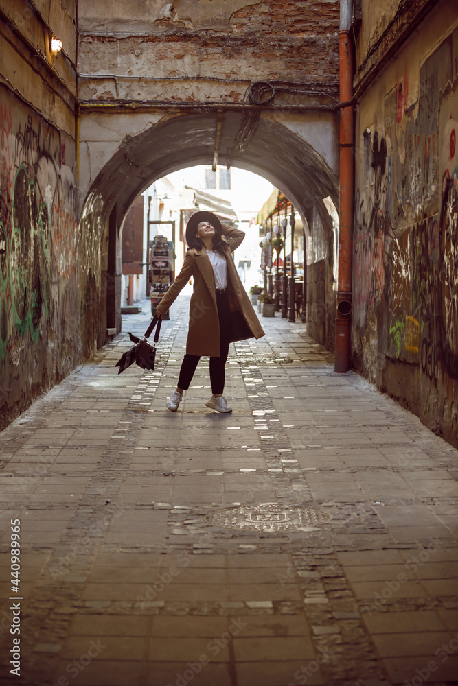 woman in stylish coat and hat walking by small european street