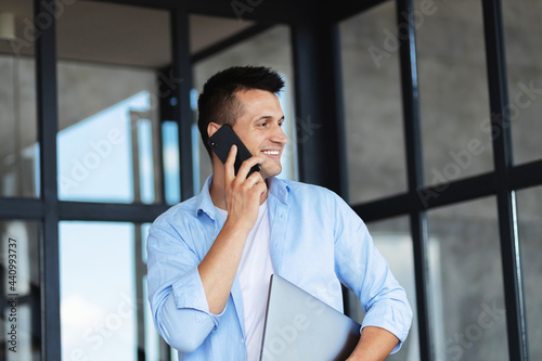 Headshot portrait of caucasian successful businessman or ceo with mobile phone and laptop standing in office, smiling