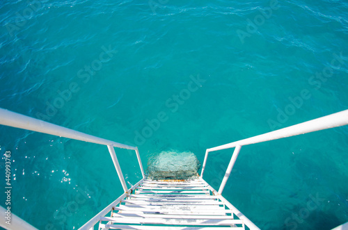 White steps from the pier into the turquoise waters of the Mediterranean. The ladder with handrails is lowered into the water for convenience of tourists. Top view of the sea surface with copy space. © ksjundra07