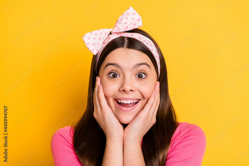 Photo of impressed sweet school girl wear pink t-shirt big eyes arms cheeks isolated yellow color background Photo of impressed sweet school girl wear pink t-shirt big eyes arms cheeks isolated yellow color background