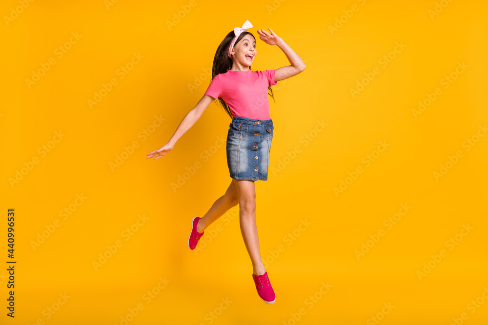 Photo of shiny excited school girl wear pink t-shirt jumping arm forehead looking far away empty space isolated yellow color background Photo of shiny excited school girl wear pink t-shirt jumping arm forehead looking far away empty space isolated yellow color background