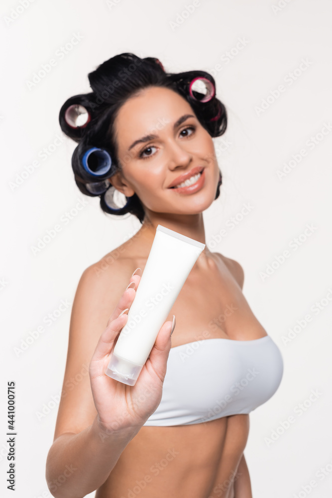 smiling young woman in curlers and bra showing cream tube isolated on white. smiling young woman in curlers and bra showing cream tube isolated on white.