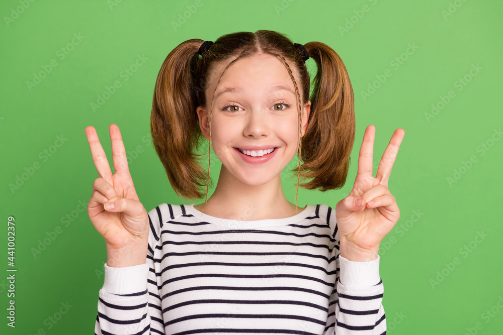 Photo of funny tails hairdo little girl show v-sign wear striped sweater isolated on green color background Photo of funny tails hairdo little girl show v-sign wear striped sweater isolated on green color background