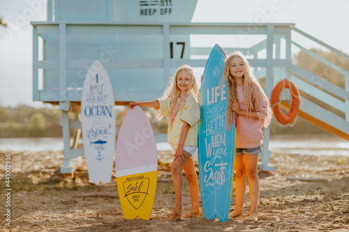 Photography Girls posing with surfboards against blue lifeguard tower on the sand beach