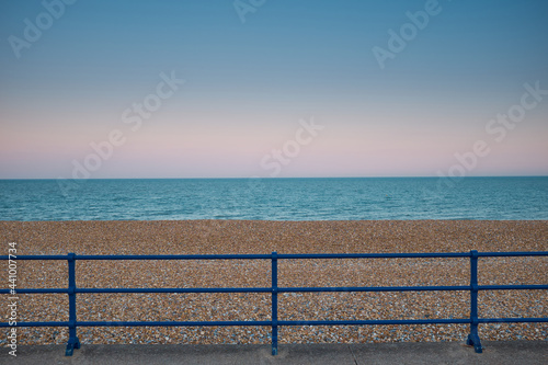 Blue painted metal railings in front of open, empty, shingle beach on Eastbourne promenade.