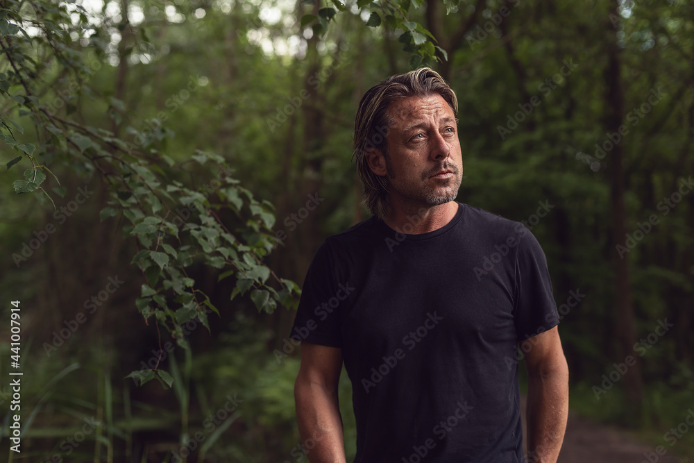Blond man with stubble beard in a black t-shirt in a lush forest. Blond man with stubble beard in a black t-shirt in a lush forest.