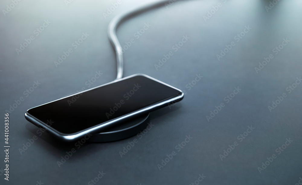 Recharging smartphone battery during workday in office. Using induction wireless charging. Grey background. Recharging smartphone battery during workday in office. Using induction wireless charging. Grey background.