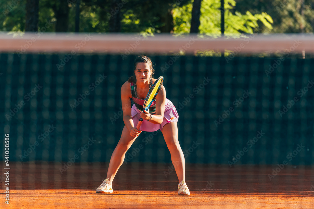 Female tennis player waiting to return serve playing a tennis game on a clay court.