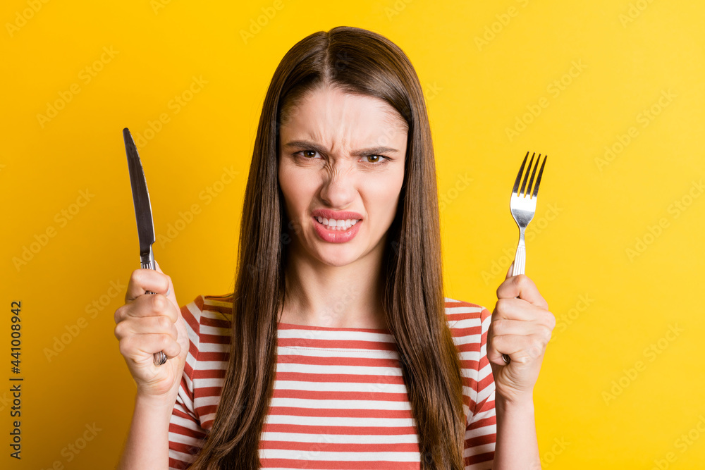 Portrait of attractive angry girl holding cutlery fast food meal snack isolated over bright yellow color background Portrait of attractive angry girl holding cutlery fast food meal snack isolated over bright yellow color background