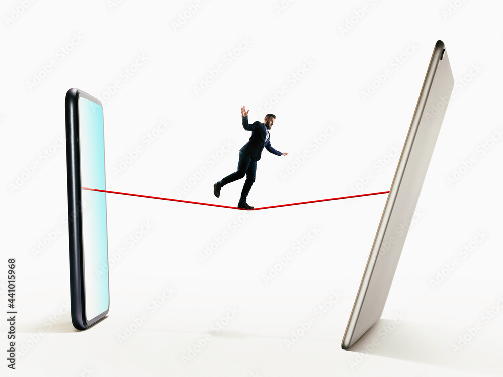 A man walks a tightrope from smartphone to digital tablet. Risk, balance concept. A man walks a tightrope from smartphone to digital tablet. Risk, balance concept.