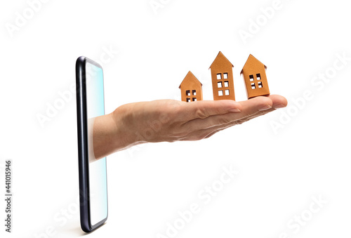 Human hand with paper houses stick out of a smartphone screen. Concept of modern technologies in real estate industry.