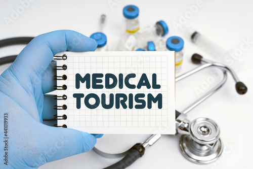 There is a stethoscope on the table, the doctor holds a notebook in his hand with the inscription - MEDICAL TOURISM