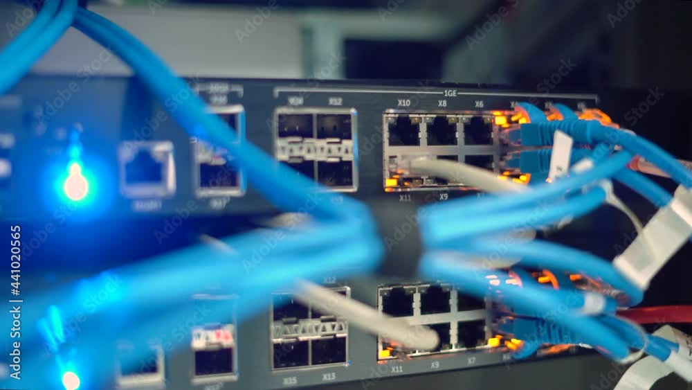 Close up network cables attached to cloud computing system with blinking lights in server room.