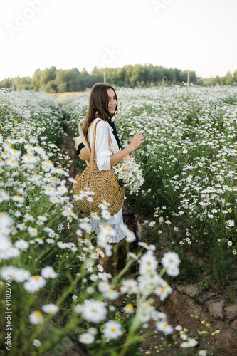 beautiful young woman in a chamomile field in a picturesque valley. young lady in cotton white dress and straw hat and spring green nature, harmony concept. the idea of self-care, a healthy lifestyle 