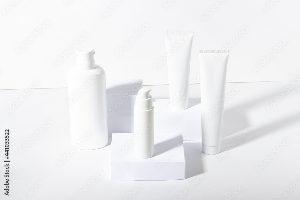 A set of white cosmetic jars on square stands with shadows. Toothpaste, face and body cream, hair shampoo. Professional cosmetics for skin care. Organic cosmetics.