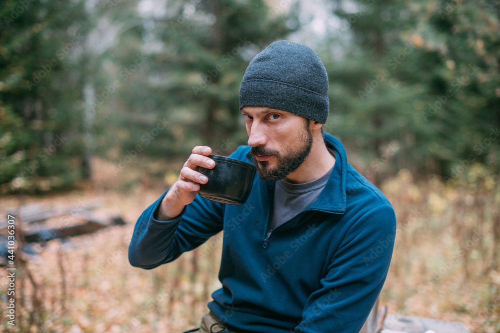 A man hiker drinks tea while resting in the forest.