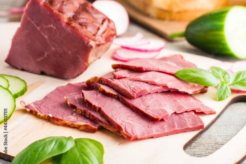Fresh sliced marbled beef pastrami and vegetables on a cutting board. American delicacy. Rustic style. Close-up Fresh sliced marbled beef pastrami and vegetables on a cutting board. American delicacy. Rustic style. Close-up