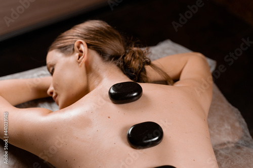 Hot stone massage therapy for relax and ease tense muscles and damaged soft tissues of body. Heated stones are placed on specific parts young woman