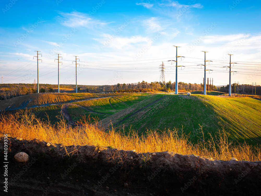 Fototapeta premium Industrial Landscape with Electricity Pylons on the Hills. Dramatic Cloudscape over Electric Poles and Cables on Blue Sky. Retro Technology Backdrop Image with Space for Text or Design