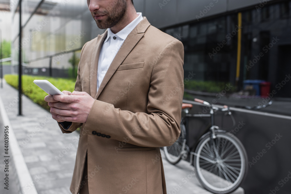 cropped view of bearded businessman using smartphone outside.