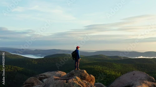 Aerial shot of a lone man on top of a mountain at dawn.
