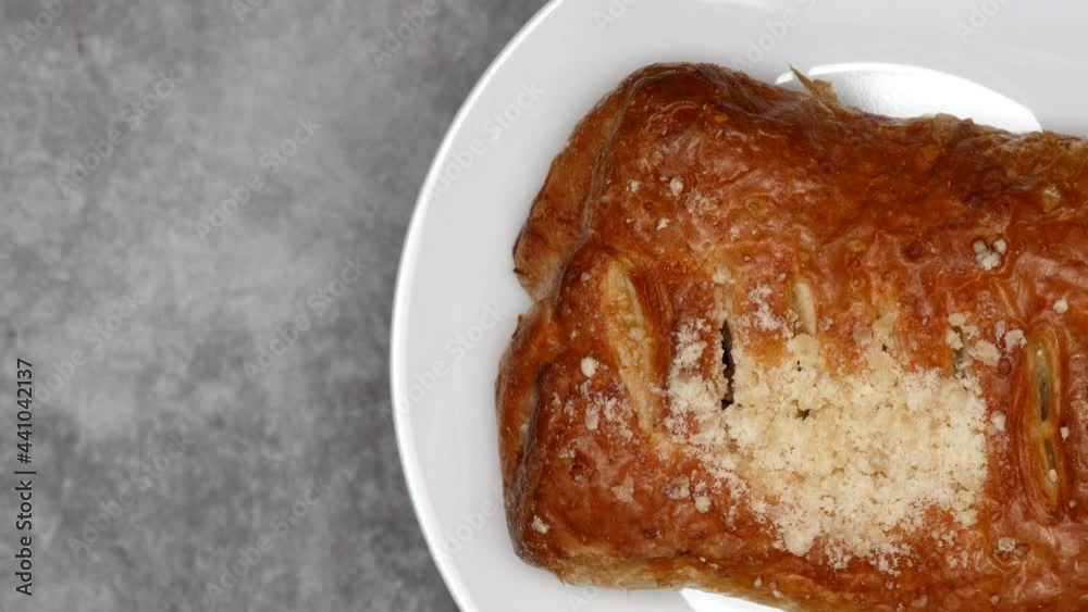 Close Up Pastry Bun On White Plate Rotating On Gray Marble Background On The Right Side. Top View. Close Up Pastry Bun On White Plate Rotating On Gray Marble Background On The Right Side. Top View.