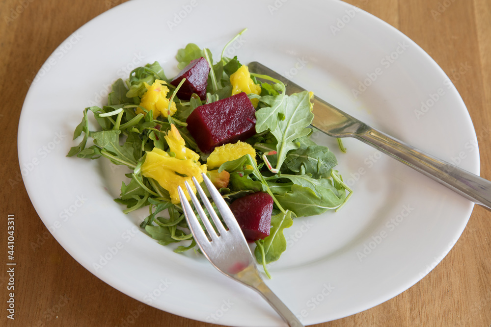 A salad of arugula and beets on white plate with knife and fork