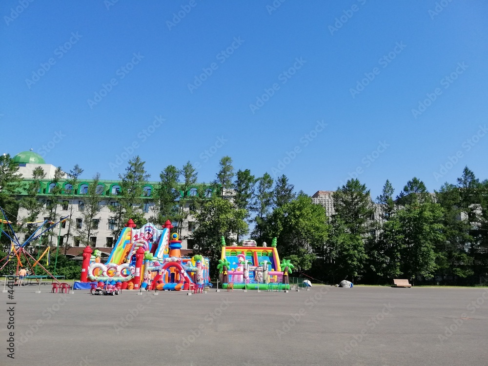 city park and square with inflatable trampolines and bouncy castle on a sunny summer day and a family with a baby in stroller city park and square with inflatable trampolines and bouncy castle on a sunny summer day and a family with a baby in stroller