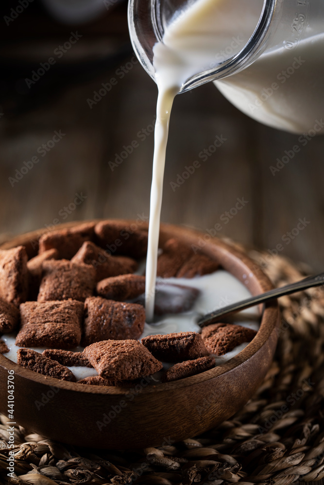 Fototapeta premium Chocolate pads, sweet breakfast cereal with chocolate filling.Milk pouring from a glass jug 