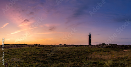 a sunset over a grassy field with a lighthouse