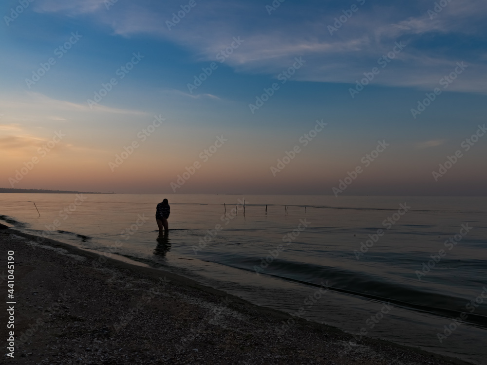 dark figure of a fisherman in the morning catches shrimp on the beach