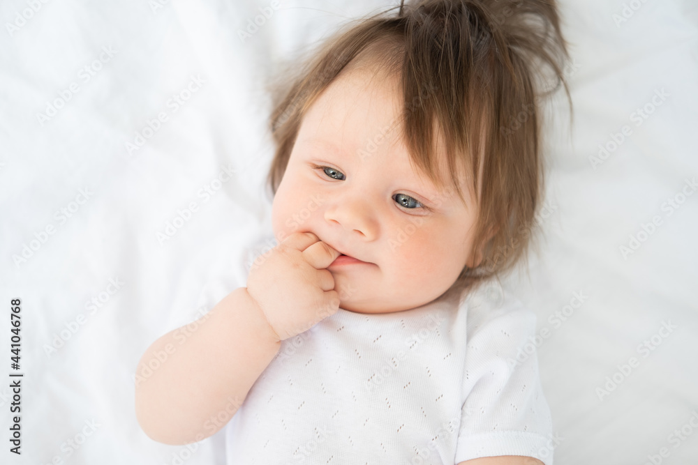 portrait of funny baby boy with finger in a mouth smiling and lying on a white bedding at home. portrait of funny baby boy with finger in a mouth smiling and lying on a white bedding at home.