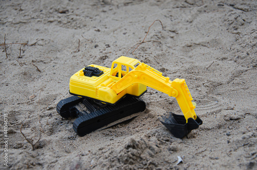 Yellow plastic excavator in the sand. Toy construction equipment. Children's toys on the beach. © Алексей Ковалев