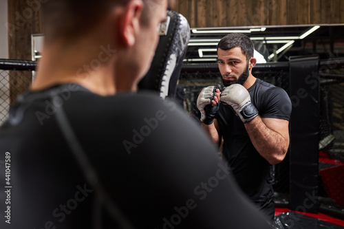 Strong Confident Fighter or Wrestler Training With Professional MMA Fighter At Gym In Ring, Preparing For Competition Together. Rear View on Man