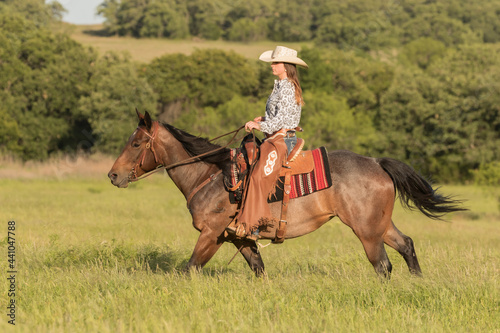 Women galloping a horse in a pasture wearing western attire 