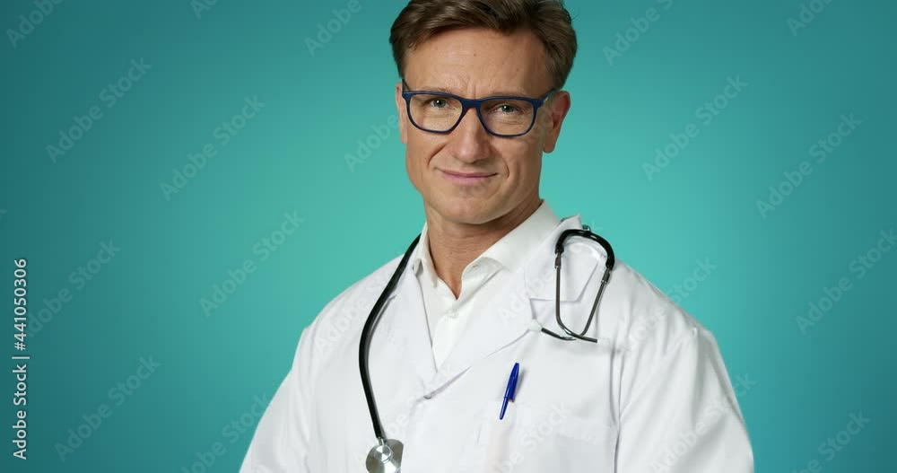 Handsome Doctor in a White Lab Coat with a Stethoscope Smiling at Camera Posing Slow Motion. Medical Professional at Clinic Looking with Positive Emotion. Closeup Face Medic Worker Healthcare Concept. Handsome Doctor in a White Lab Coat with a Stethoscope Smiling at Camera Posing Slow Motion. Medical Professional at Clinic Looking with Positive Emotion. Closeup Face Medic Worker Healthcare Concept.
