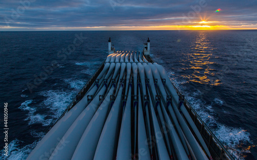 Transportation of blades for wind turbines on a cargo ship across the ocean at sunset.