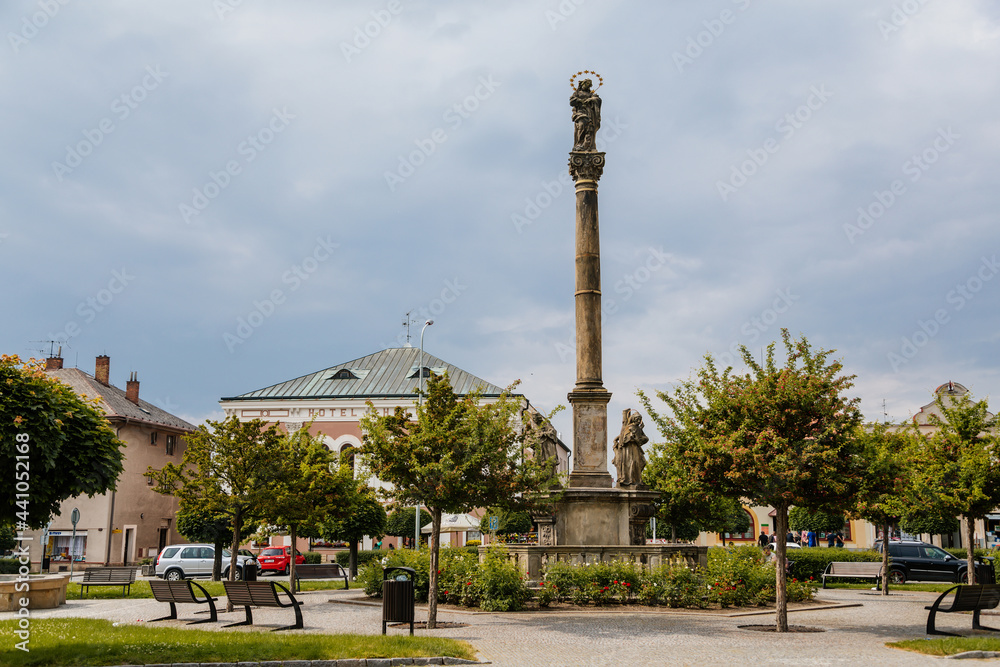 Marian Column at Kupkovo square, cobble stone street, historic center in medieval town, green lawn, trees, benches for rest, summer sunny day, Opocno, Czech Republic