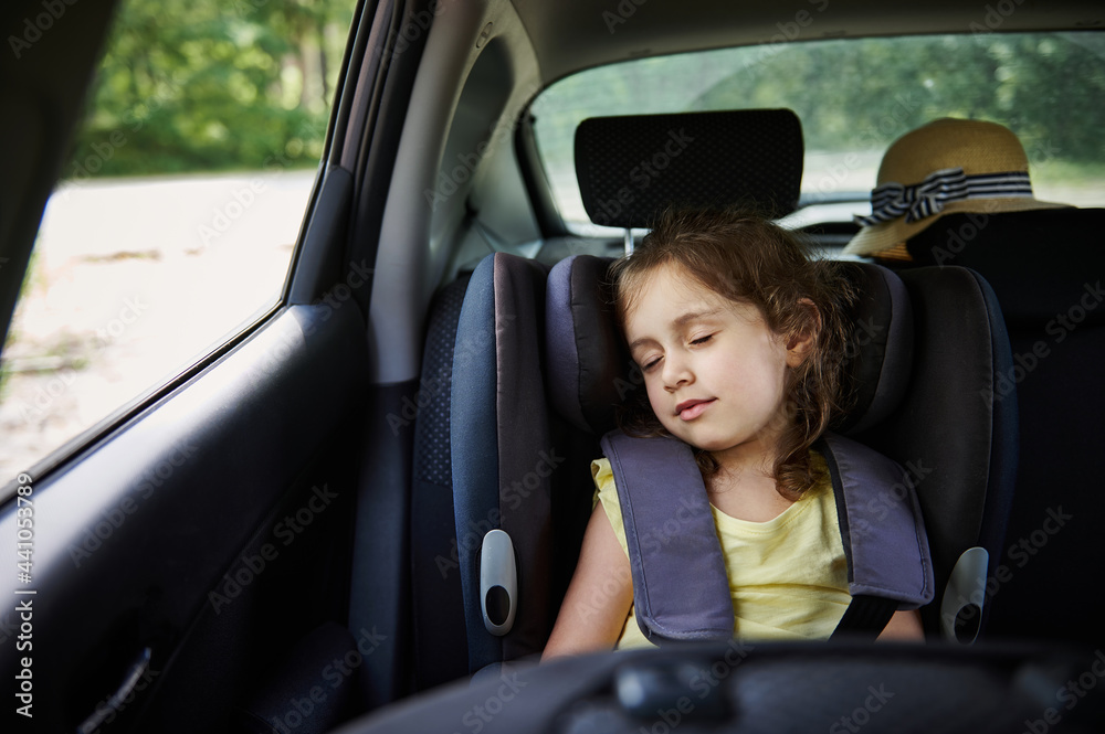 Safe movement of children in the car. Little girl sleeps in a booster seat in the car. Child safety seat.