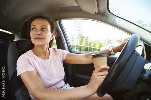 Young unfastened woman driver looking to the side while driving a car and drinking coffee from a takeaway cup © Taras Grebinets