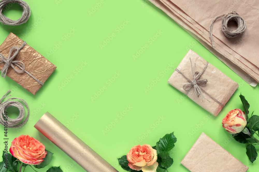 Gift boxes in wrapping paper, tied with rope, with bouquet of red-yellow roses for congratulations on green background. Creative holiday present. Gift boxes in wrapping paper, tied with rope, with bouquet of red-yellow roses for congratulations on green background. Creative holiday present.