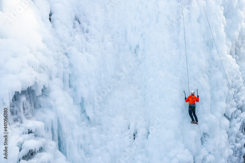Male athlete doing a vertical ice climb, kicking front crampons into the ice and swinging an ice tool