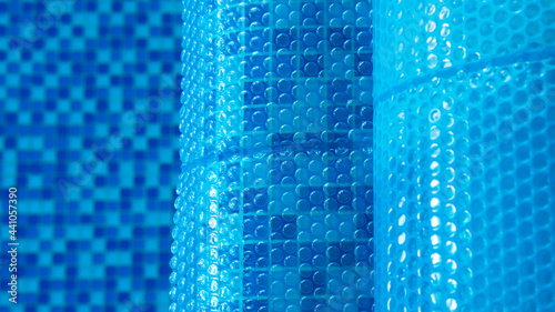 Blue tarpaulin pool cover. Bubble awning wrap for swimming pool cover. Swimming pool with a blue water. Close up. Top view. Selective focus.