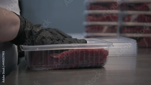 Butcher in black proective gloves prepares fresh meat for delivery to stores. Different cuts of fresh raw beef meat in trays on table in slaughterhouse. Slow motion. Meat production and food industry, photo