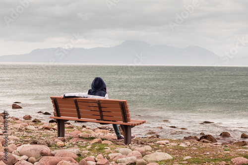 Wallpaper Mural Teenager girl sitting on a bench and enjoys view on Atlantic ocean, low cloudy sky. Croagh Patrick in the background. Travel and tourism concept Torontodigital.ca