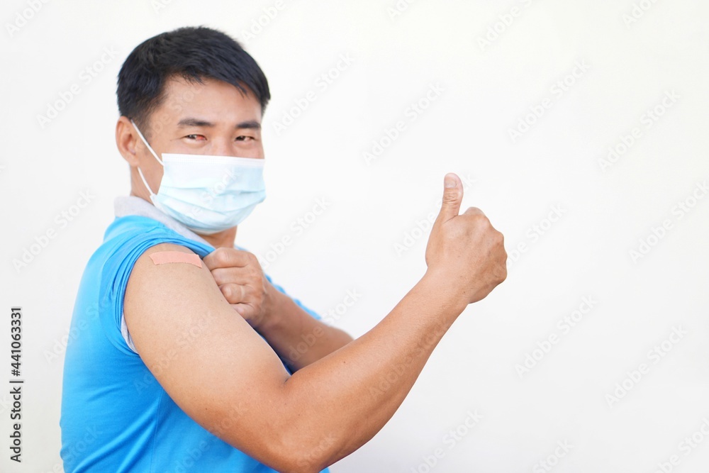 Concept : Covid-19 vaccination campaign. Handsome Asian man wears hygienic face mask and shows adhesive bandage plaster on his shoulder after got vaccinated, raise thumb up. Concept : Covid-19 vaccination campaign. Handsome Asian man wears hygienic face mask and shows adhesive bandage plaster on his shoulder after got vaccinated, raise thumb up.