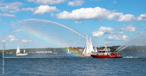 Firefighting ship demonstrating its reach and creating a rainbow. Sunny day on the water with white fluffy clouds in a bright blue sky. Tall Ships Festival, Brockville, Ontario, Canada