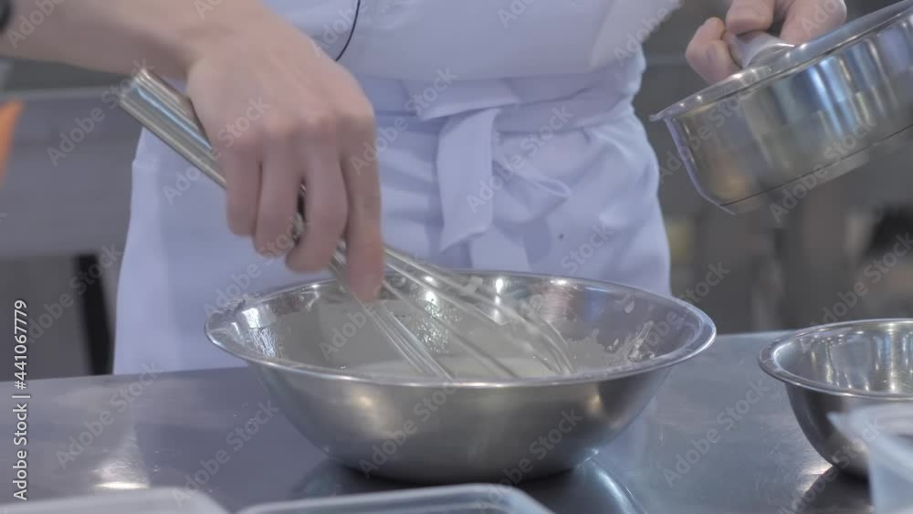 Close up: baker, chef hands holding balloon whisk and preparing whipped sweet cream in steel bowl on kitchen table at cuisine of restaurant. Cooking, bakery, gastronomy and food concept Close up: baker, chef hands holding balloon whisk and preparing whipped sweet cream in steel bowl on kitchen table at cuisine of restaurant. Cooking, bakery, gastronomy and food concept