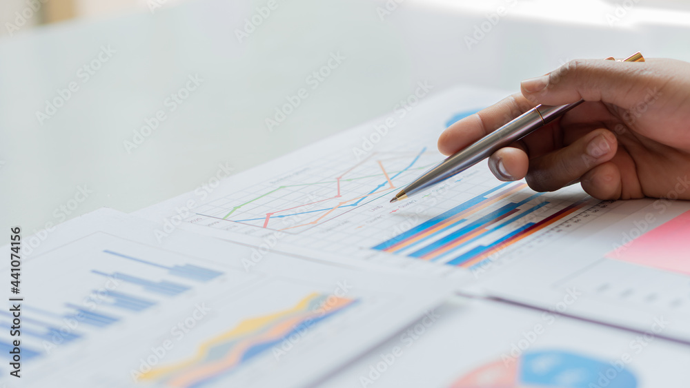Businessman studying statistics and analyzing pens and graphing documents on a desk with a laptop and a calculator Businessman studying statistics and analyzing pens and graphing documents on a desk with a laptop and a calculator